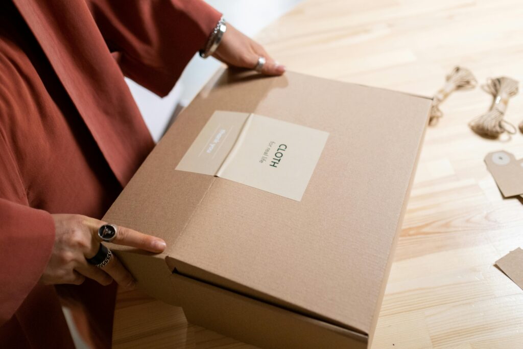 Close-up of a woman packing a cardboard box on a wooden table indoors.